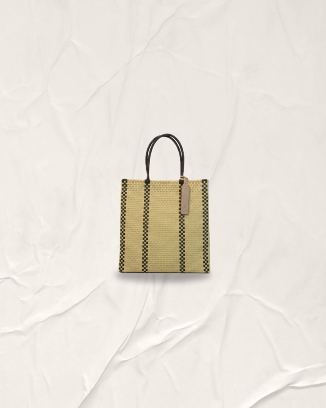 Hand-woven Pilar Bag in Serene Cream with two vertical Anchor Black lines on each side. Medium-sized tote with cream handles, crafted from recycled plastic. This sustainable Indonesian bag features a vertical architectural design and is washable and foldable
